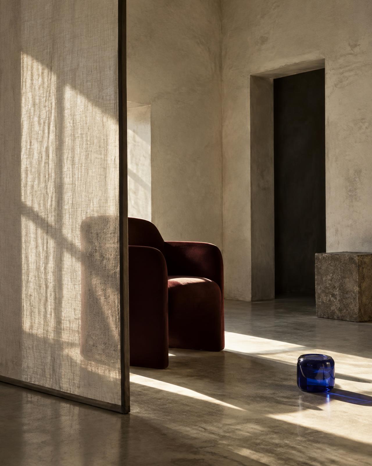 An oxblood chair behind translucent linen in an artistic, sunlit interior